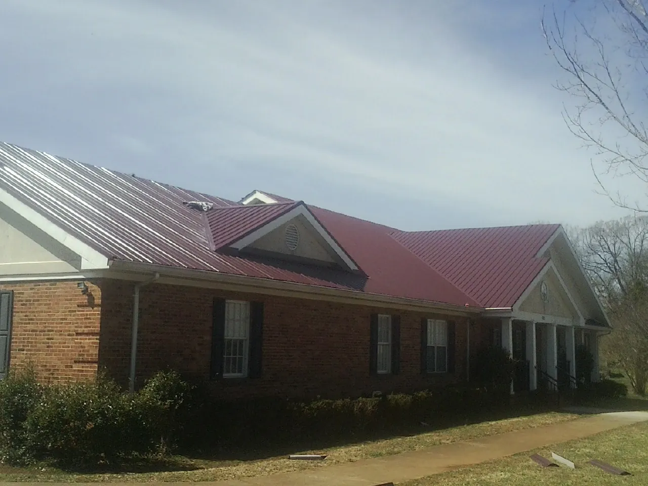 Red metal roof with gabled entries on a long brick building, from a Hail Damage Roof Repair job in Clinton